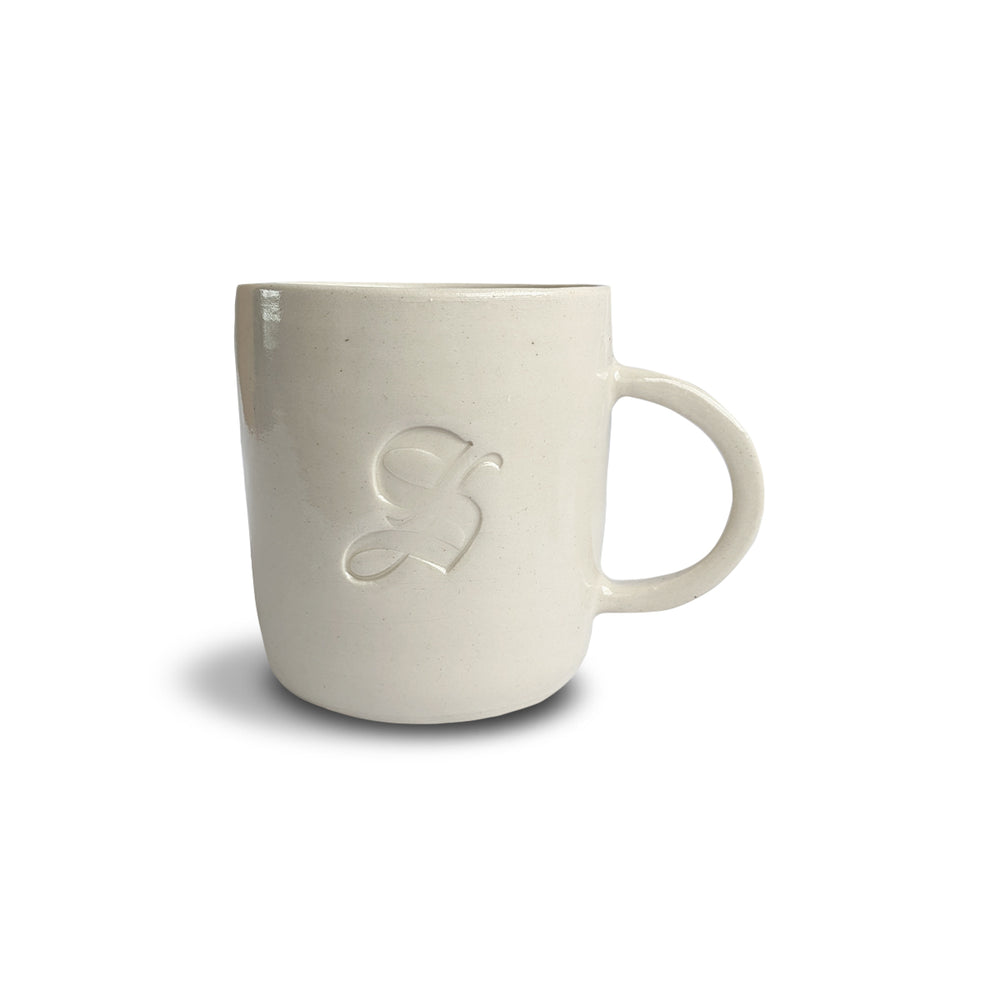 A beige ceramic mug with an embossed logo on the side, with a handle on the right side.